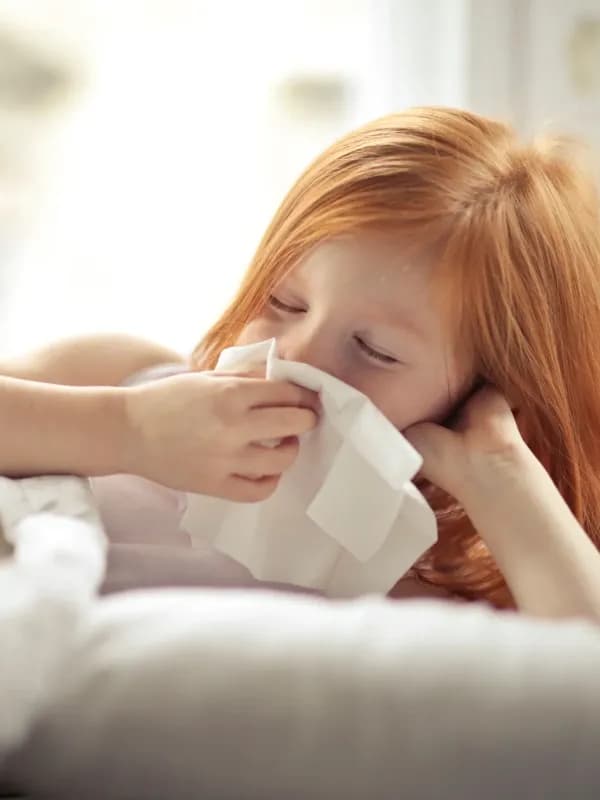 Niña con rinitis alérgica usando un pañuelo